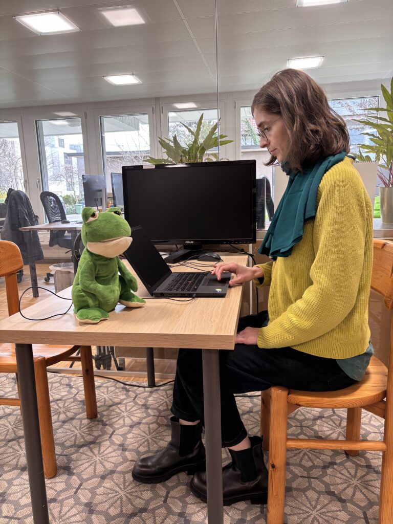 Elea vor ihrem Laptop, daneben der plüschige Frosch-Screenreader.