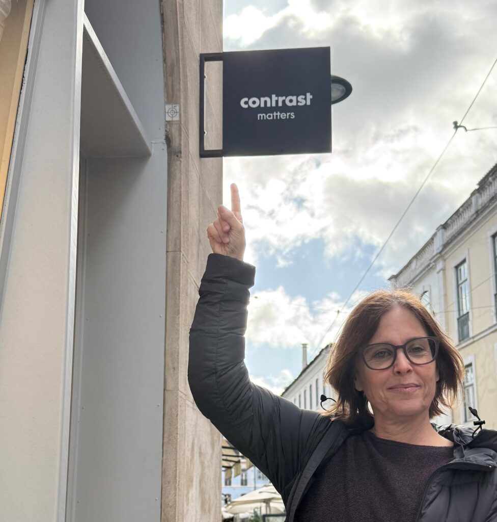 Marion zeigt auf ein Ladenschild über ihrem Kopf mit der Aufschrift «Contrast matters».